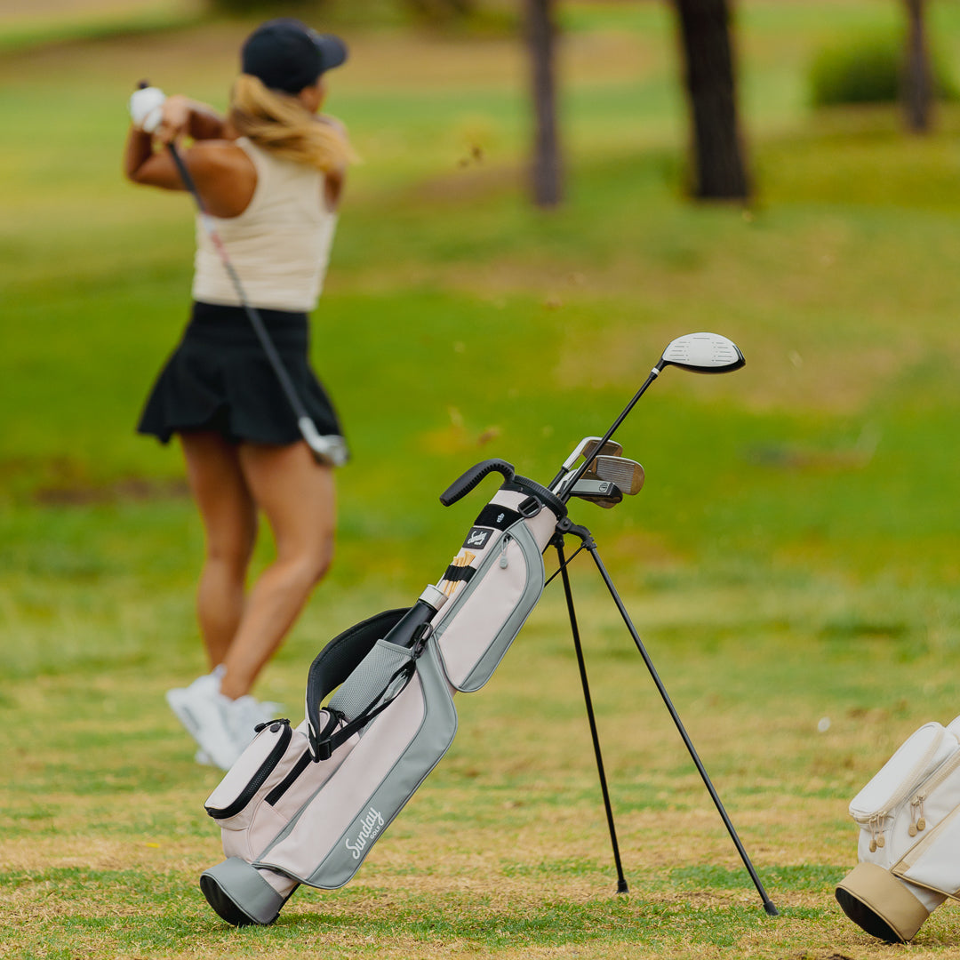 A woman golfing with a Loma golf bag in flamingo pink behind her