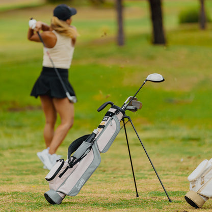 A woman golfing with a Loma golf bag in flamingo pink behind her