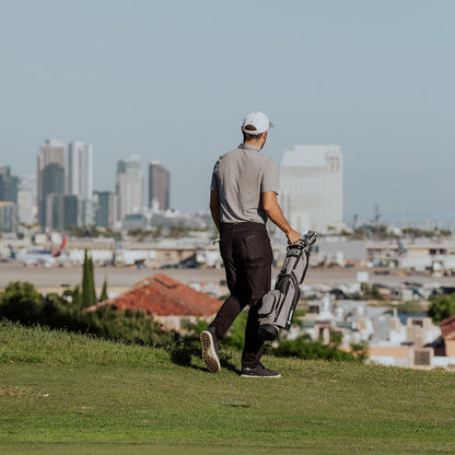 A golfer carrying a heather gray Loma golf bag with one hand