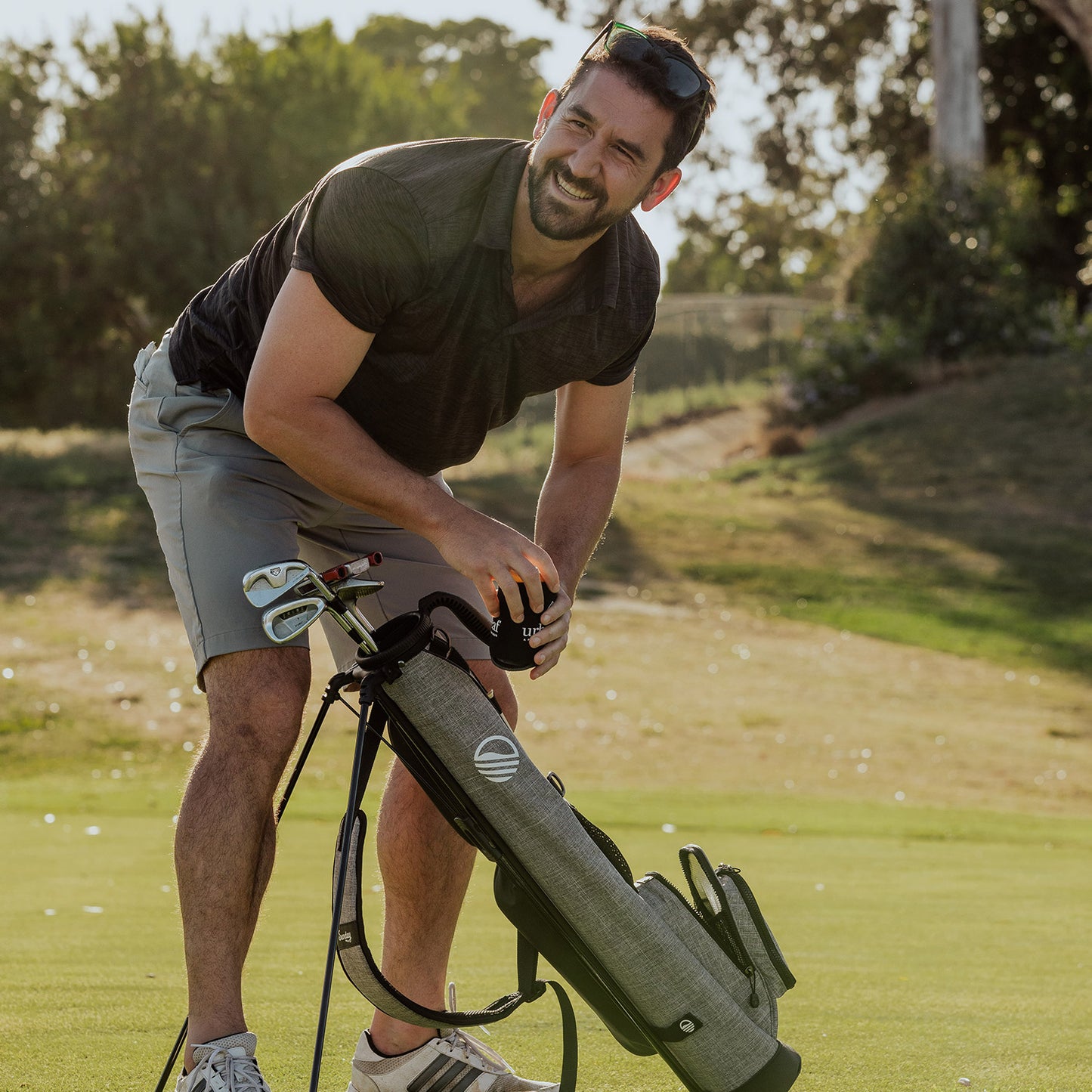 A man arranging his heather gray Loma golf bag on the course