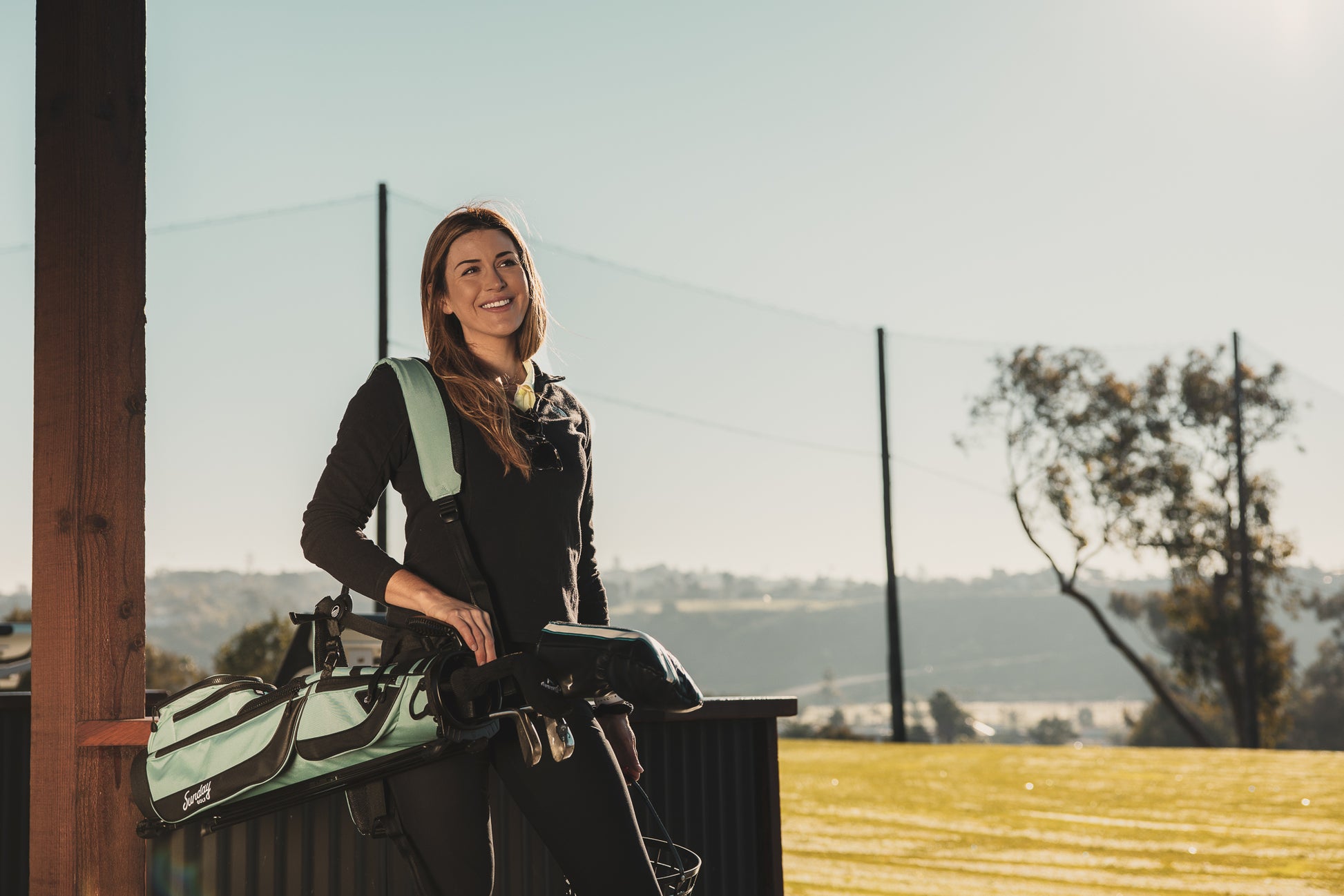 A woman carrying a seafoam Loma XL golf bag on her side