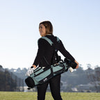 A woman carrying a seafoam green Loma XL golf bag on the course using double shoulder strap 