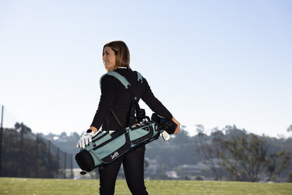 A woman carrying a seafoam green Loma XL golf bag on the course using double shoulder strap 