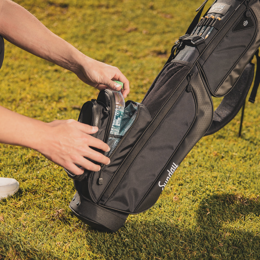 A bottled water being taken out of the insulated beverage pouch of a matte black Loma XL golf bag