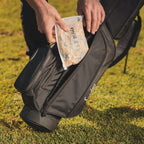 A tee bag of bamboo golf tees being placed inside a black golf bag
