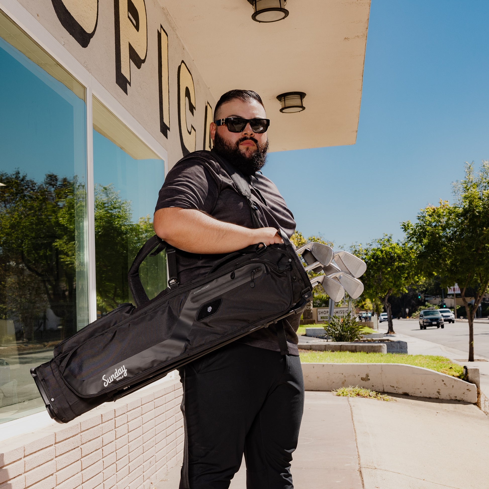 A man facing the camera, carrying El Camino golf bag in matte black