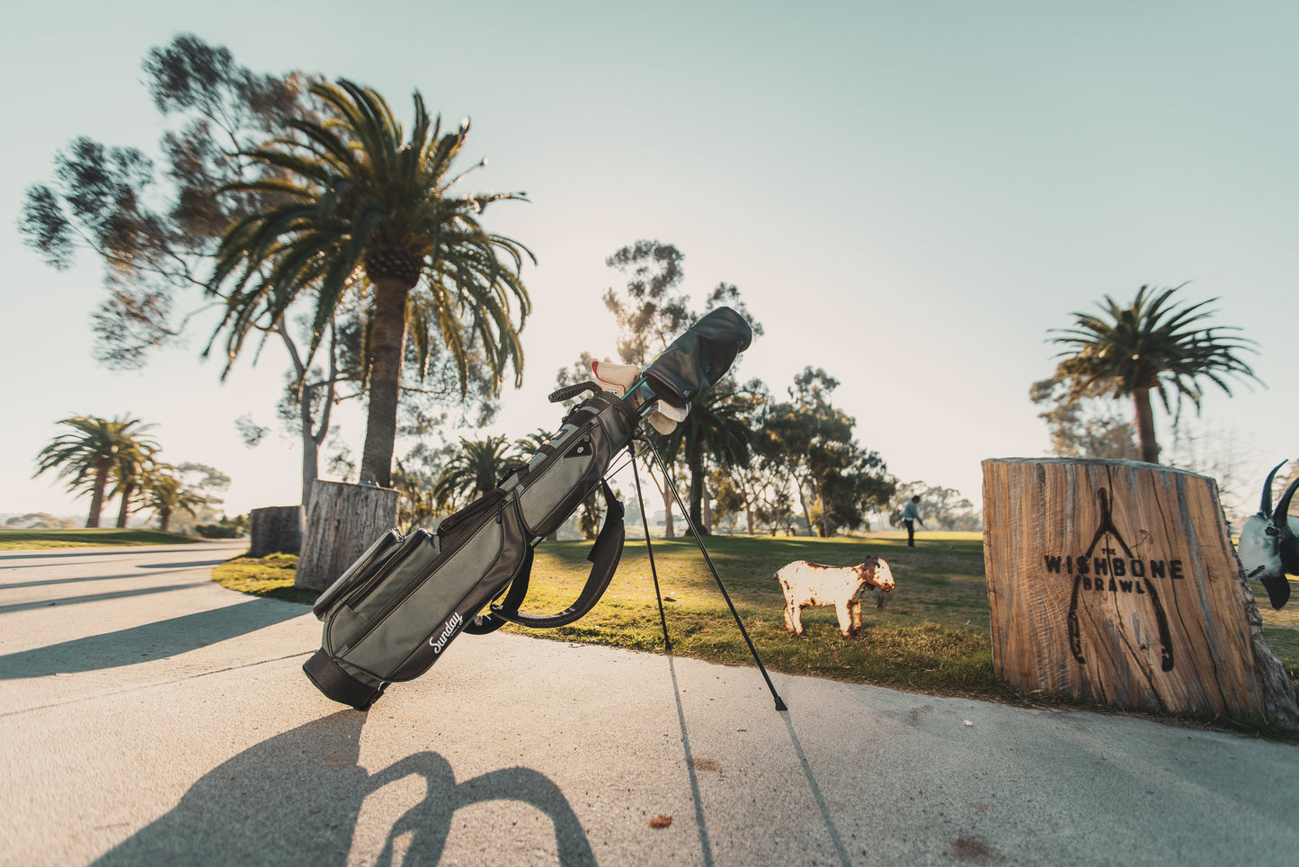 A full front shot on the course of standing Loma XL golf bag in midnight green with double strap and with palm trees in the background