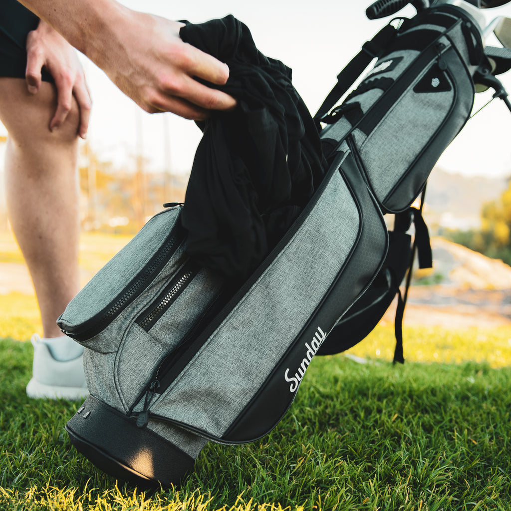 A jacket being pulled out of the storage pouch on the Loma XL golf bag in heather gray