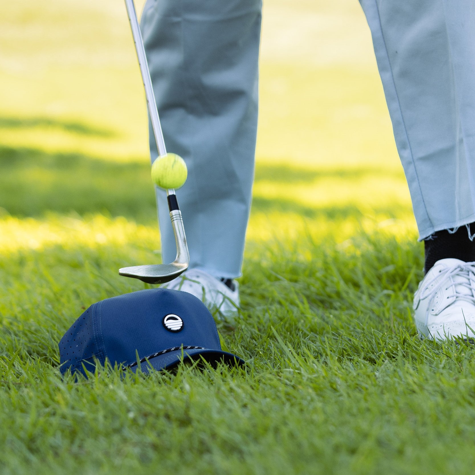 bouncing golf ball on club with the porter lite golf hat in navy on the ground