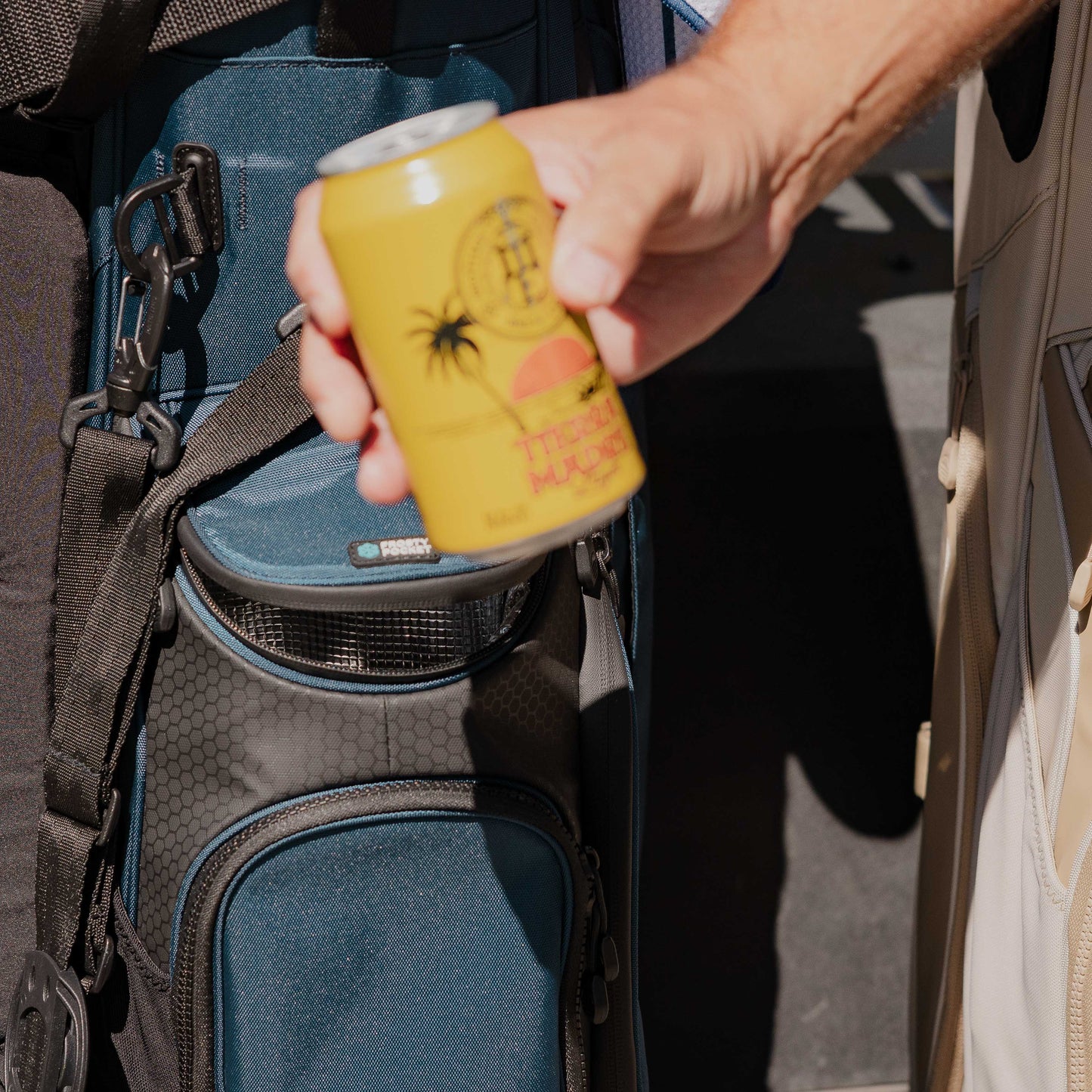 A canned drink being held up with a Ryder golf bag in navy blue in the background