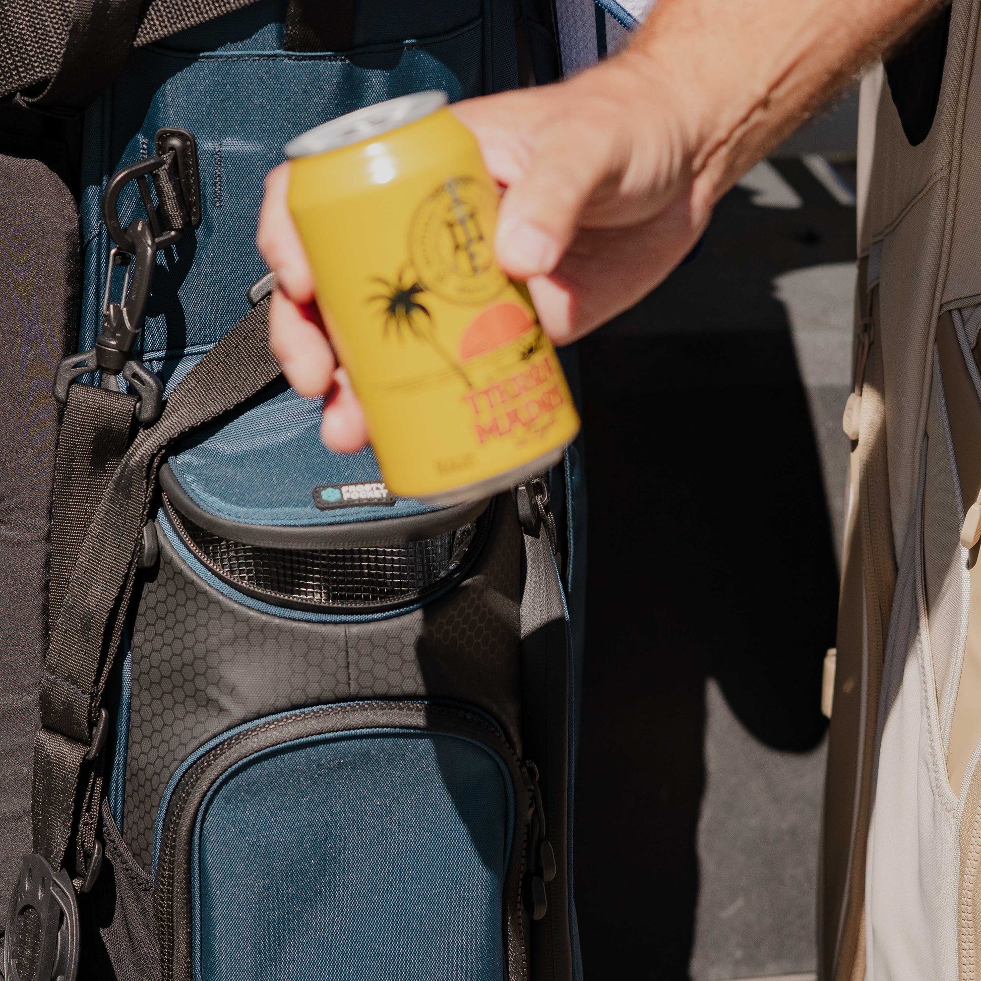 A canned drink being held up with a Ryder golf bag in navy blue in the background