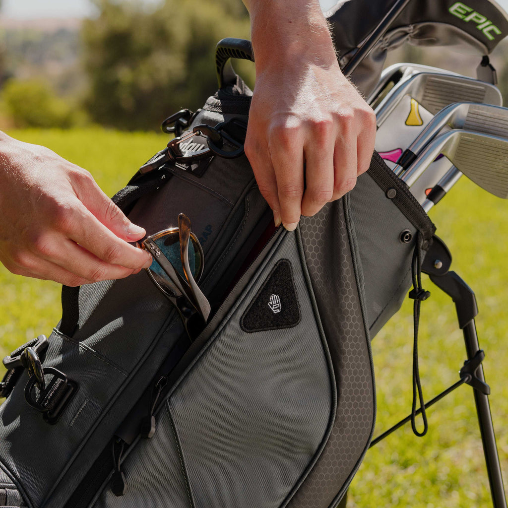 Shades being placed inside a midnight green Ryder golf bag's side pouch