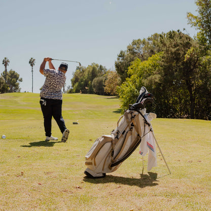 A man playing golf with his Ryder golf bag in toasted almond behind him