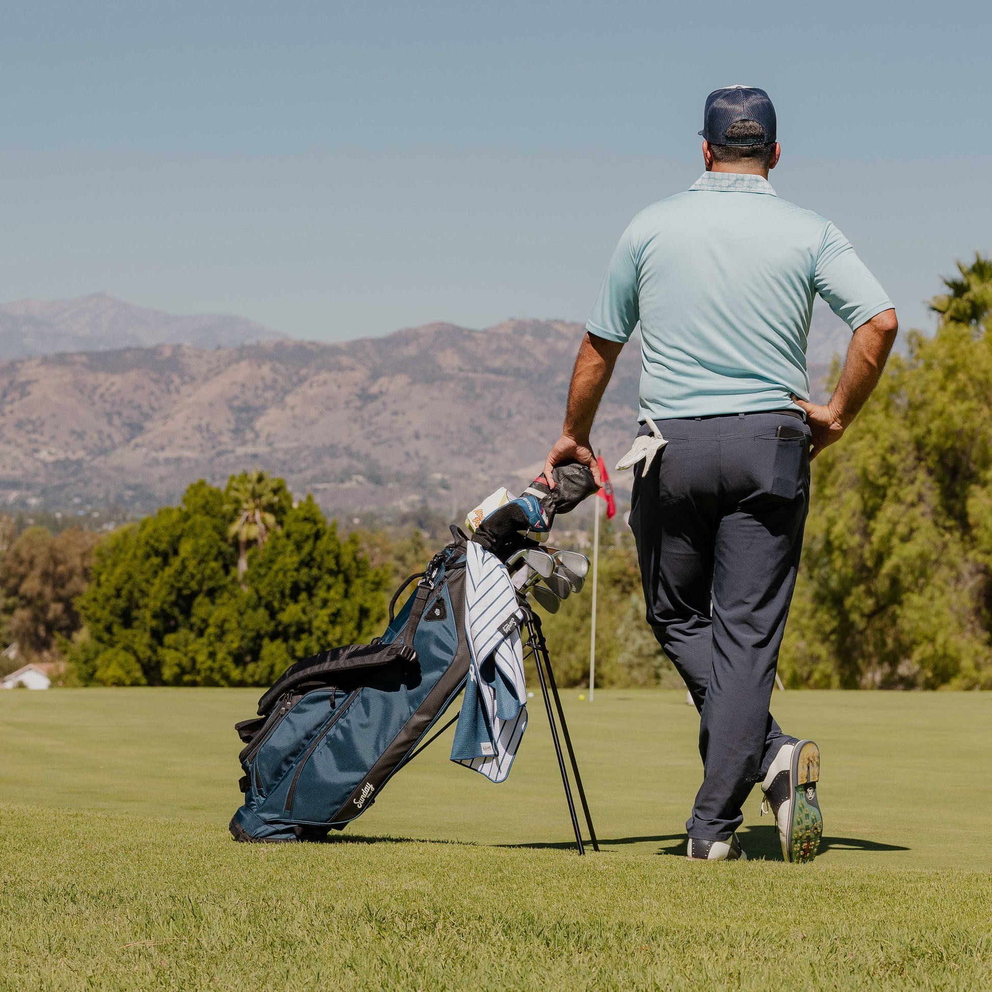 A man standing beside a Ryder golf bag in navy blue on the course