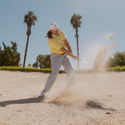 A man in sand trap wearing tropical rope golf hat while playing