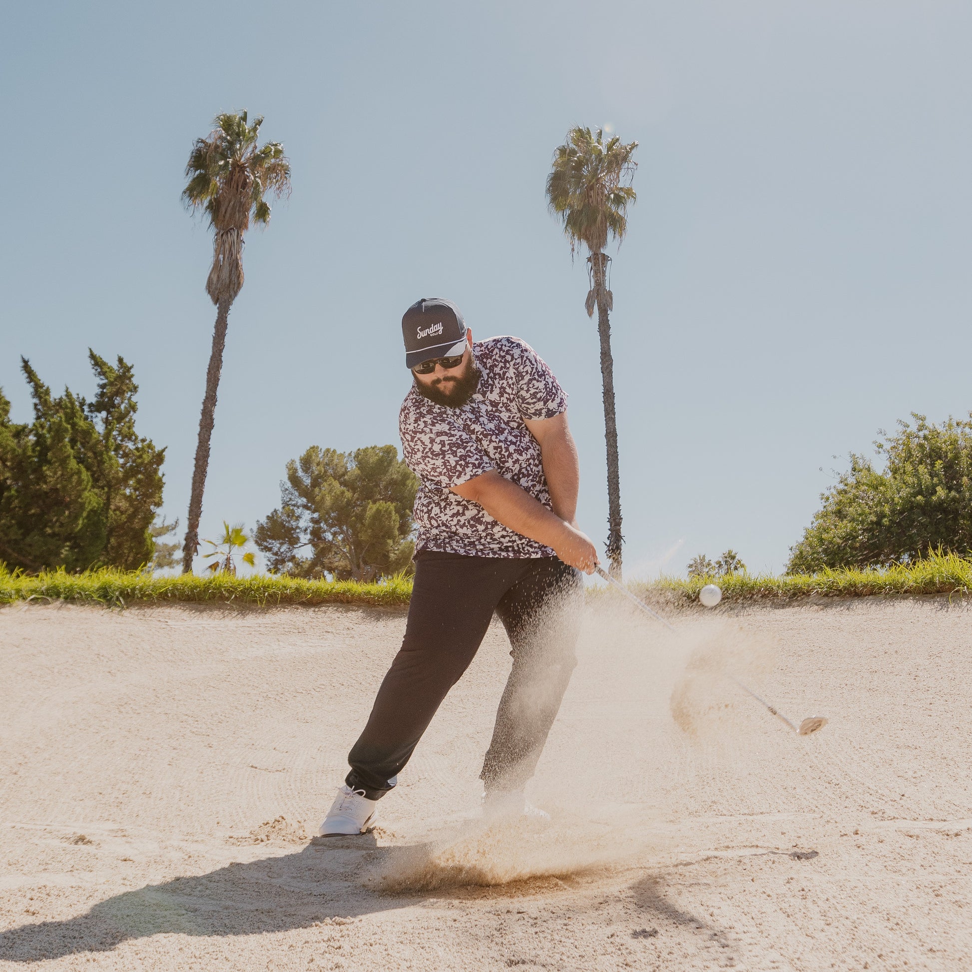 A man in sand trap with navy rope golf hat while playing