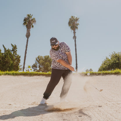 A man in sand trap with navy rope golf hat while playing