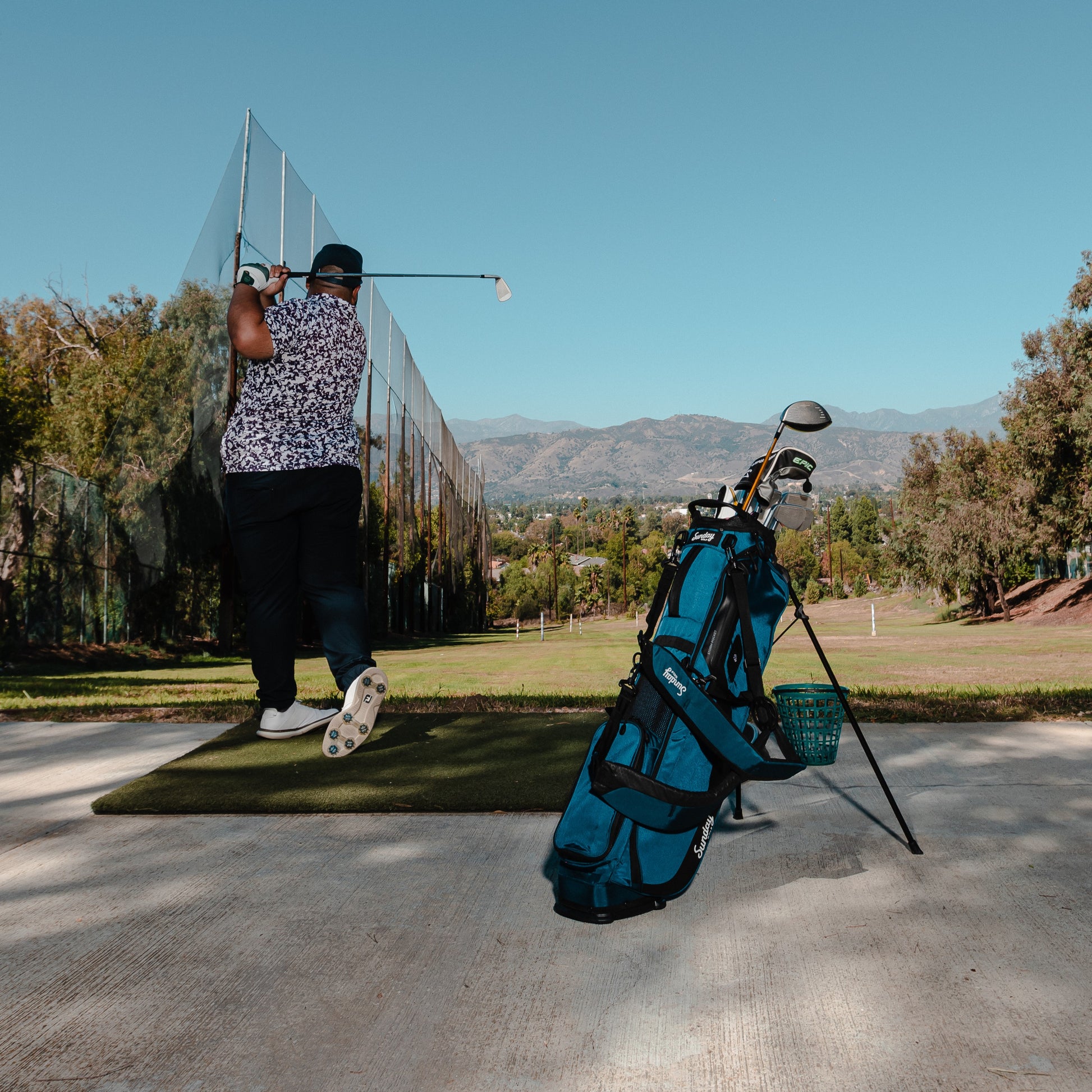 A man teeing off on the course beside a standing El Camino golf bag in cobalt blue